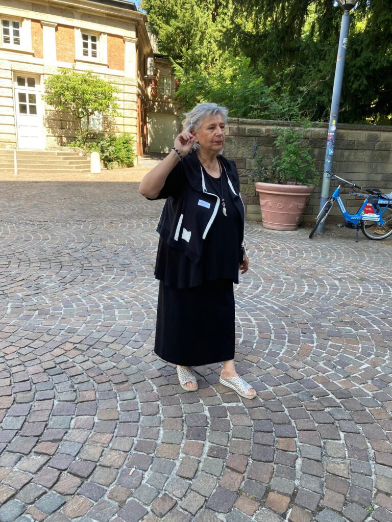 Eine Frau in schwarzer Kleidung auf einem Kopfsteinpflaster. Hinter ihr ein schönes Gründerzeitgebäude